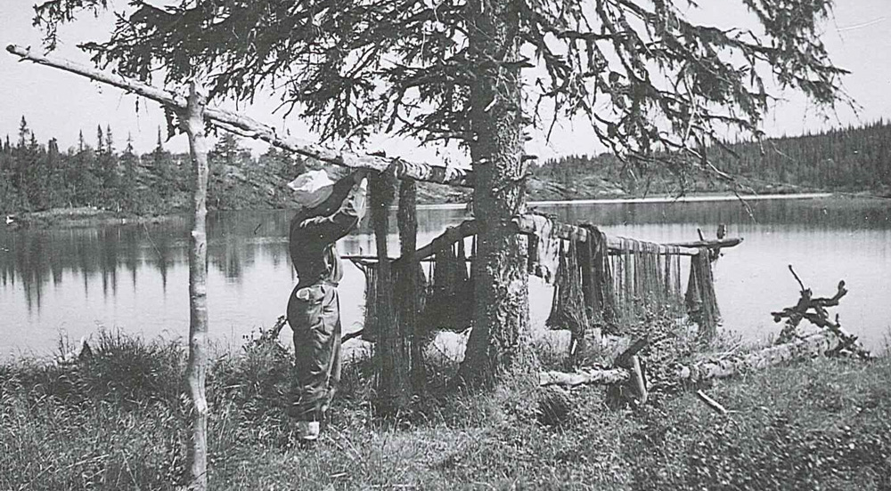 Person som står vid en sjö och hänger upp nät på en träställning.