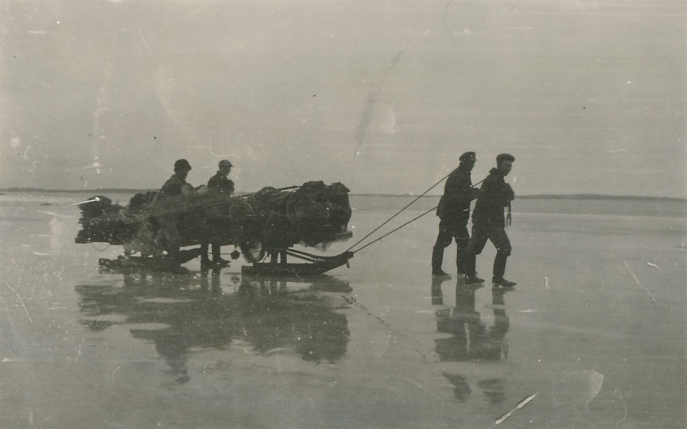 Svartvitt fotografi. Grupp män som drar en släde över isen.