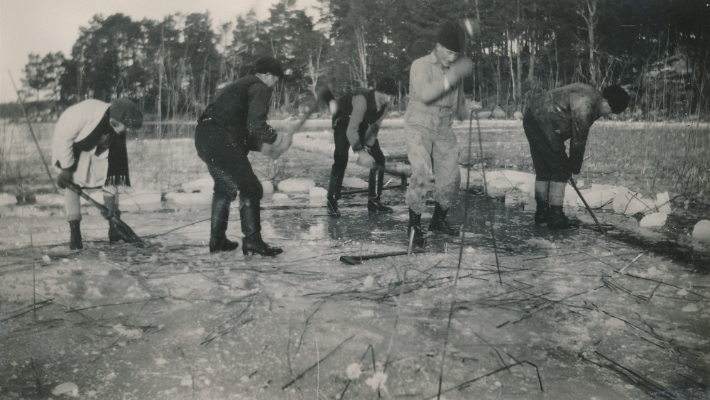 Svartvitt fotografi. Fem män som står på isen och stöter i isen med störar och verktyg.